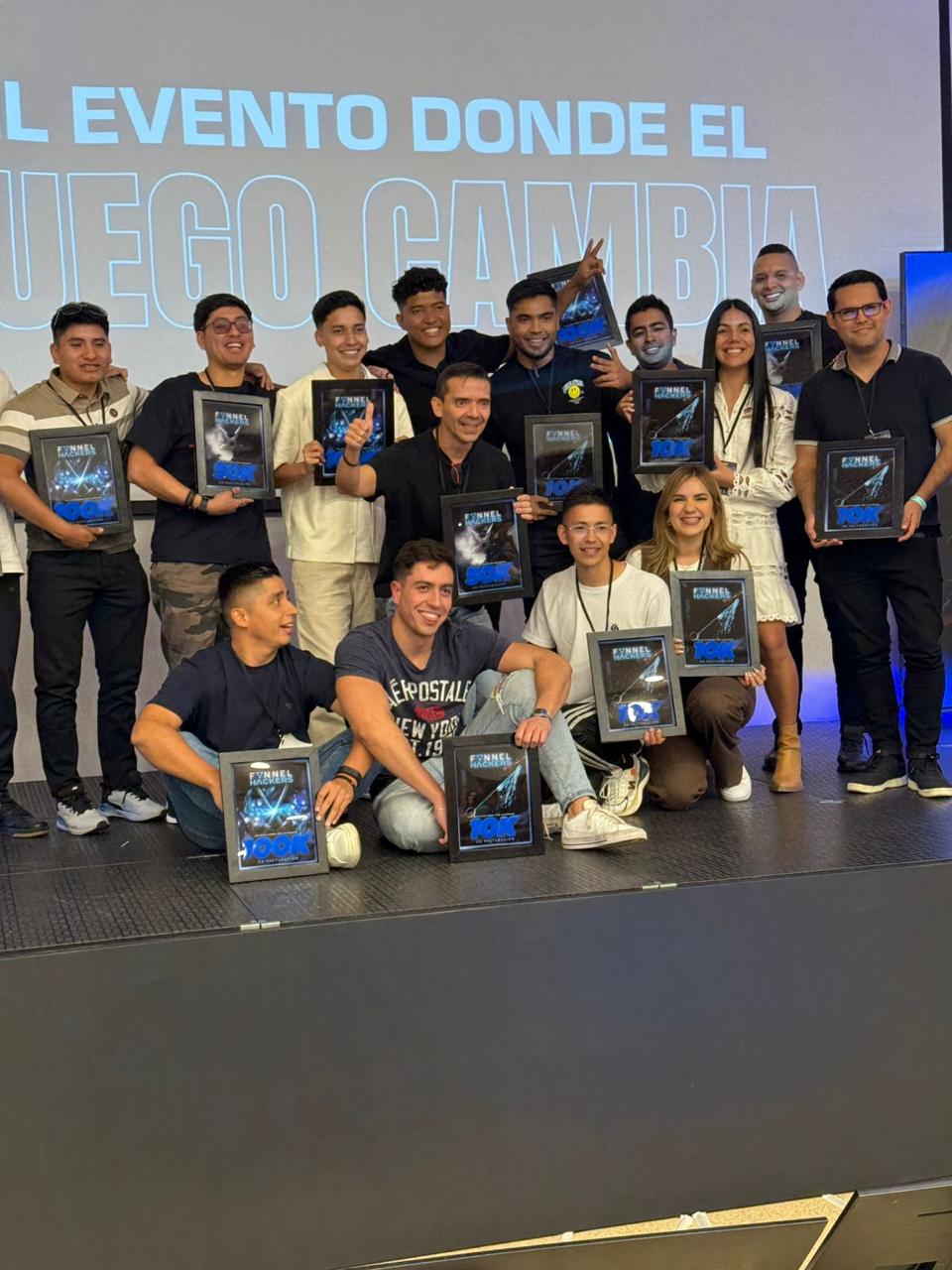 Alumnos de Juan Londoño en el evento Funnel Hackers sosteniendo placas de reconocimiento por facturación 10K, 50K y 100K.